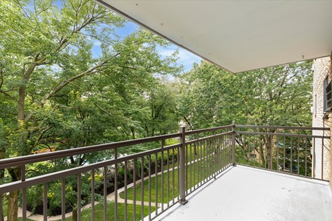 A balcony with a metal railing and a view of a tree-filled area.