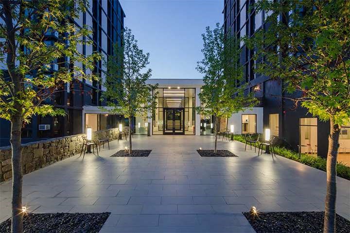 A modern building entrance with a stone wall and trees on either side.