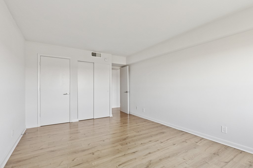A room with white walls and wood flooring with a door on the left and two closets.