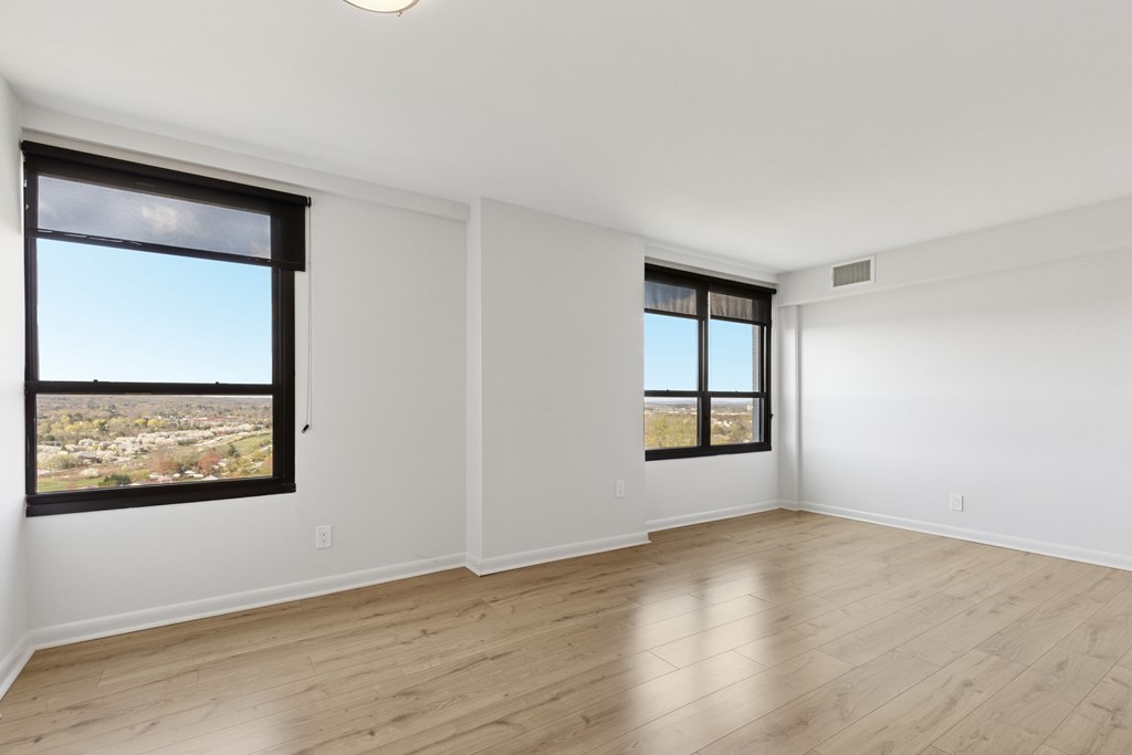 Empty room with two windows and wooden flooring.