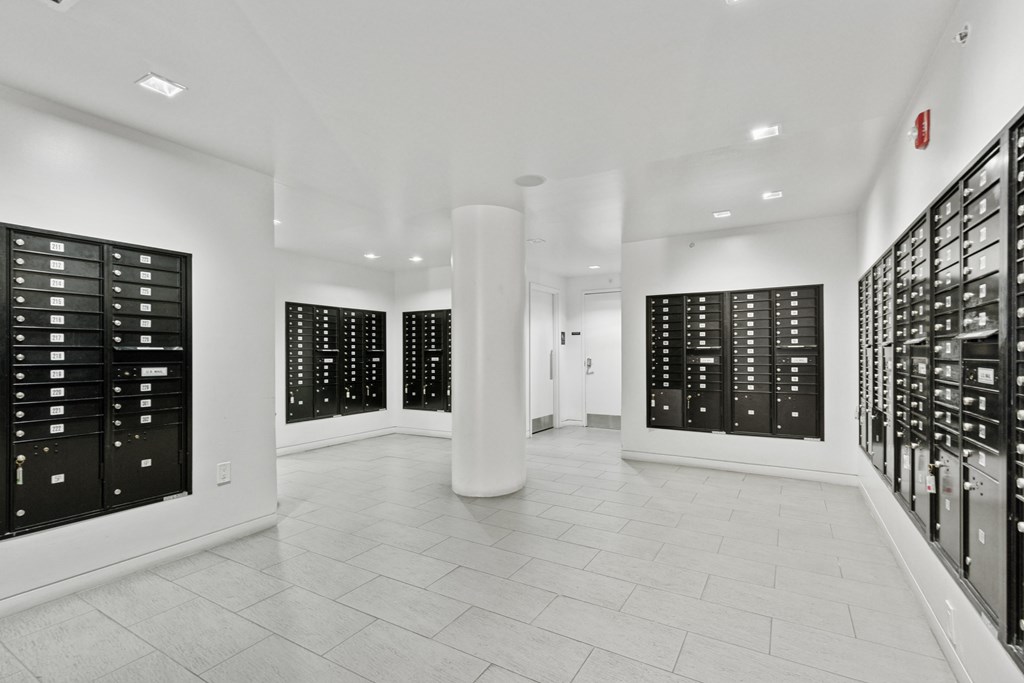 A white hallway with black lockers on the side and a white pillar in the middle.