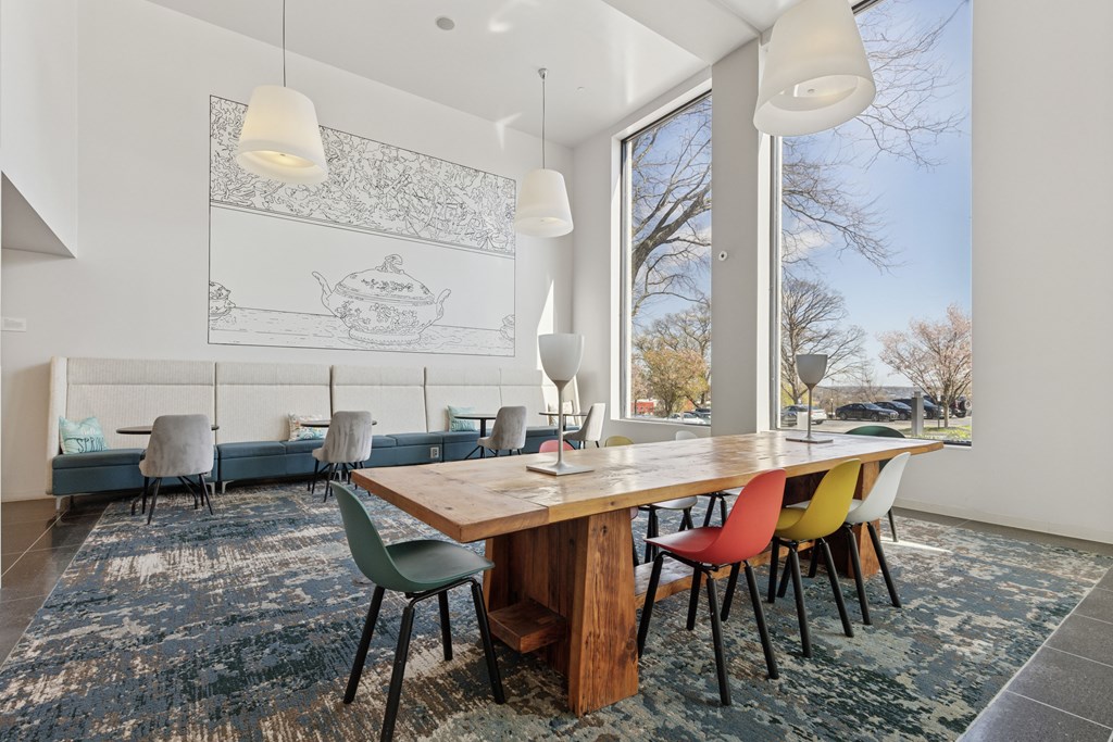 Bright and stylish west lobby at 251 Dekalb Apartments in King of Prussia, PA, featuring a communal wood table with colorful chairs, oversized pendant lights, and wall art—ideal for resident gathering or remote work.