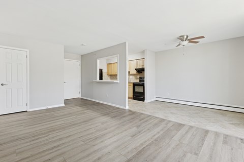 A room with a white ceiling and a wooden floor with a breakfast window looking into the kitchen.