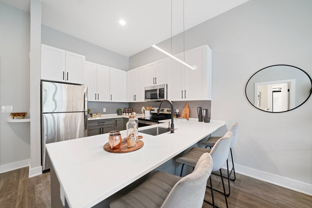 A modern kitchen with a white island and white chairs.