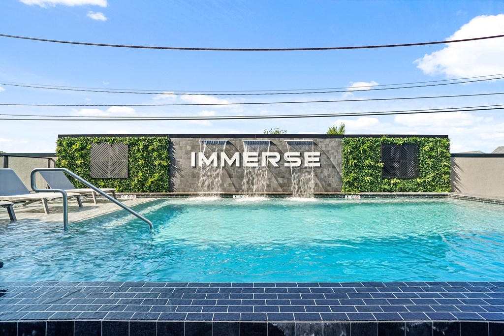 A pool with a sign that says "IMMERSE" in front of a wall of green plants.