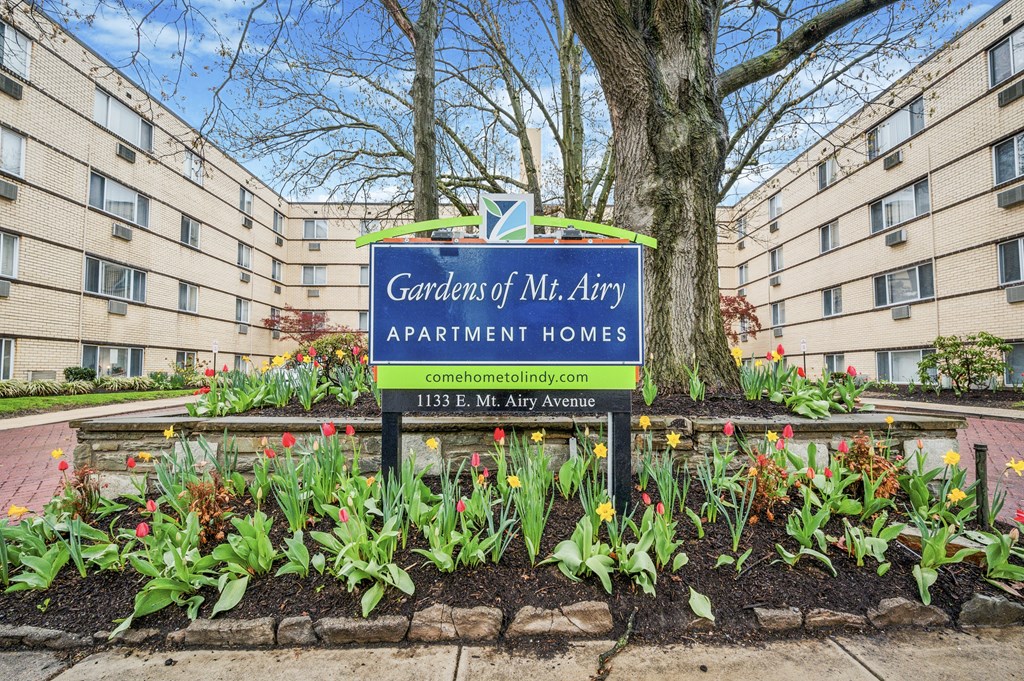 A sign for Gardens of Mr. Arry Apartment Homes is in front of a building.