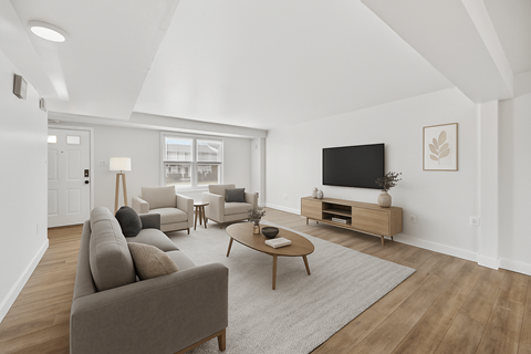 A living room with a grey couch, a coffee table, a television, and a large window.
