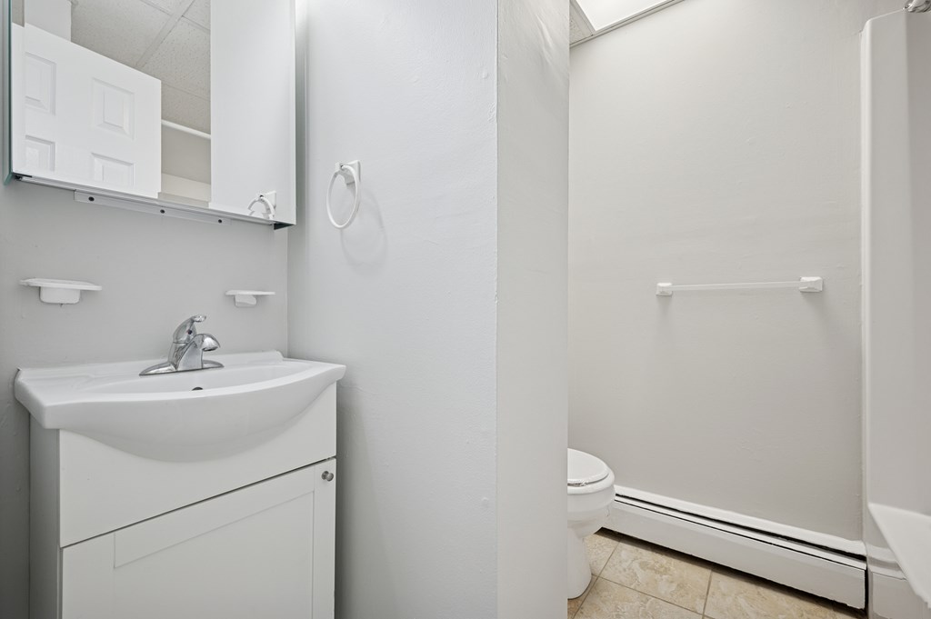 A white bathroom with a sink, mirror, and toilet.