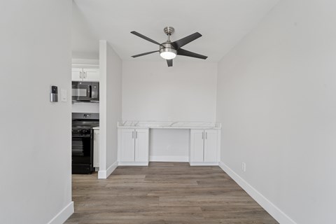 A room with a ceiling fan and a kitchen area in the background.