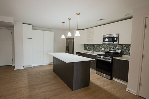 Bright modern kitchen at 251 Dekalb Apartments in King of Prussia, PA, featuring a large island with pendant lighting, stainless-steel appliances, white cabinets, and mosaic tile backsplash.