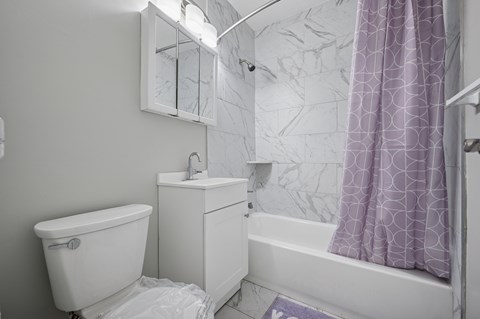 A white bathroom with a purple shower curtain.