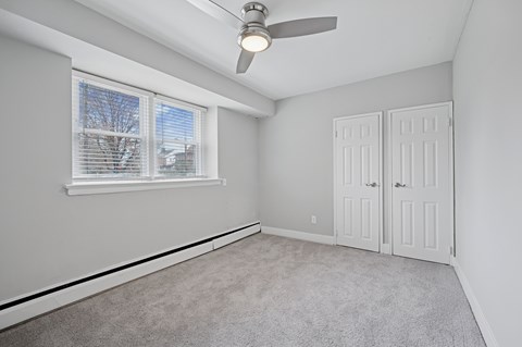 A room with a window, a ceiling fan, and two doors.