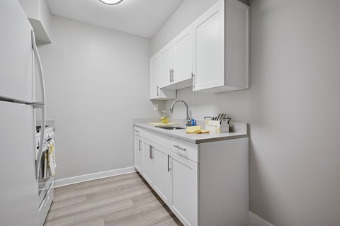 A small kitchen with white cabinets and a white fridge.