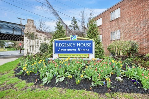A sign for Regency House Apartment Homes is in front of a brick building.