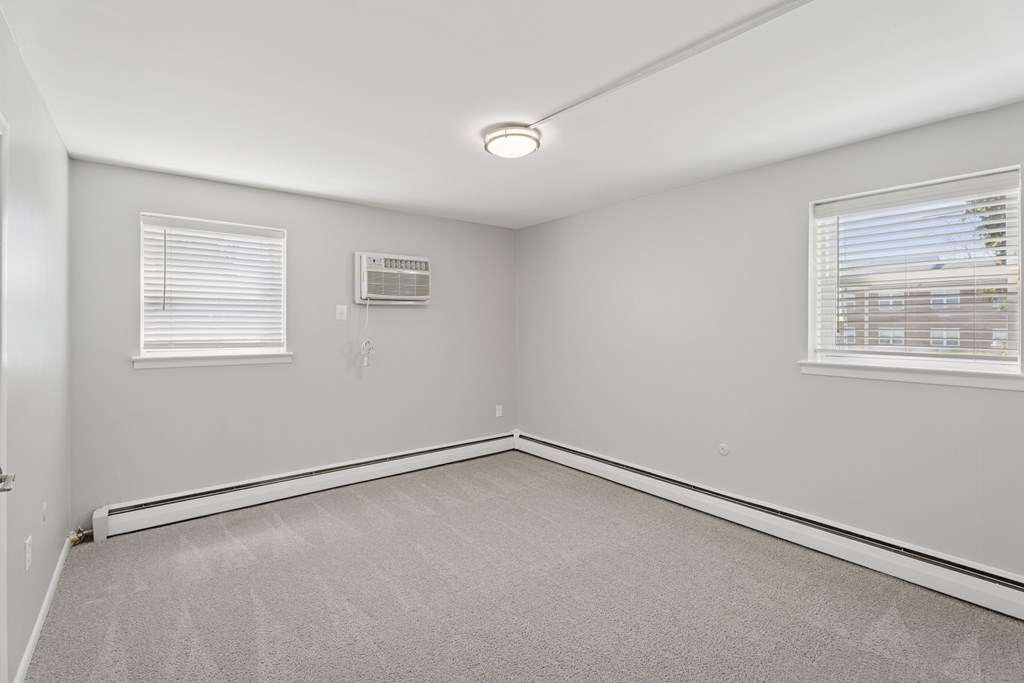 A room with a carpeted floor and two windows with blinds.