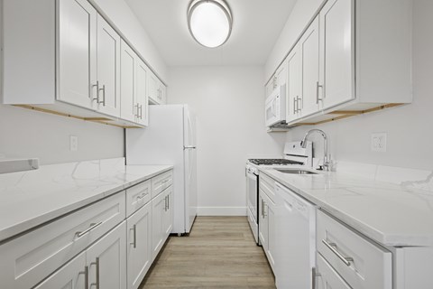 A white kitchen with a refrigerator, stove, and sink.