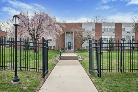 A black iron fence surrounds a building with a tree in front of it.