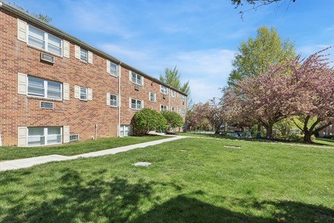 A grassy area in front of a brick building with trees.