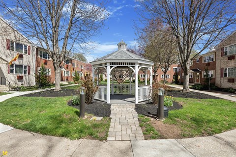 A gazebo is surrounded by a small garden and a metal fence.