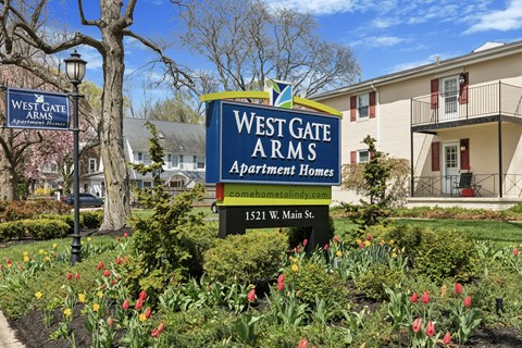 A sign for West Gate Arms Apartment Homes sits in front of a building.