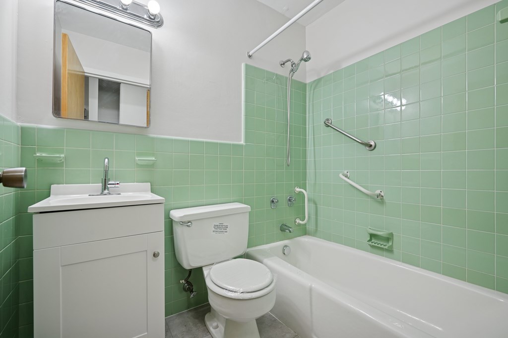 A white toilet sits next to a bathtub in a green tiled bathroom.
