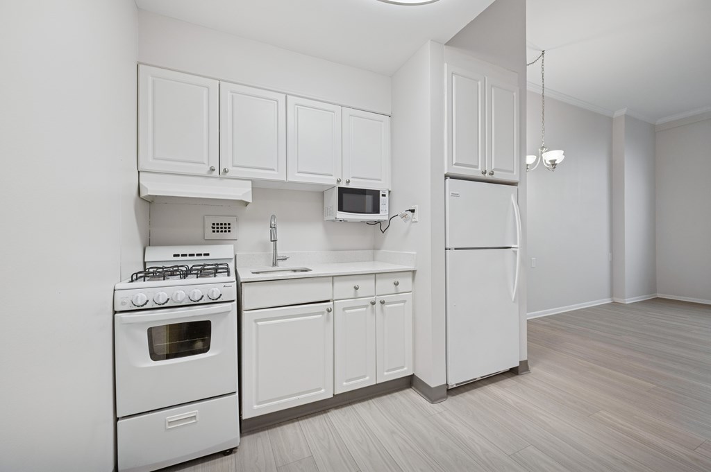 A white kitchen with a refrigerator, microwave, oven, and sink.