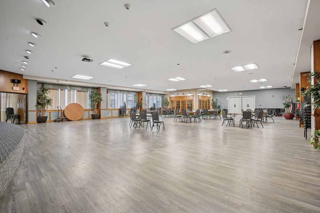 A spacious room with wooden floors and multiple chairs and tables.