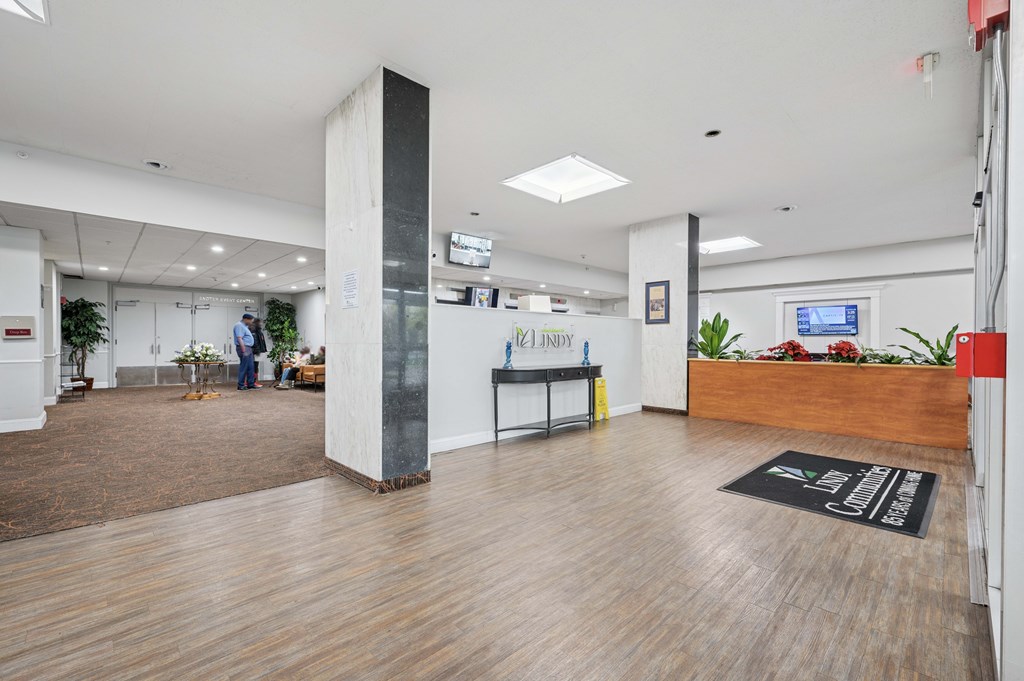 A reception area with a wooden desk and a person standing by a plant.