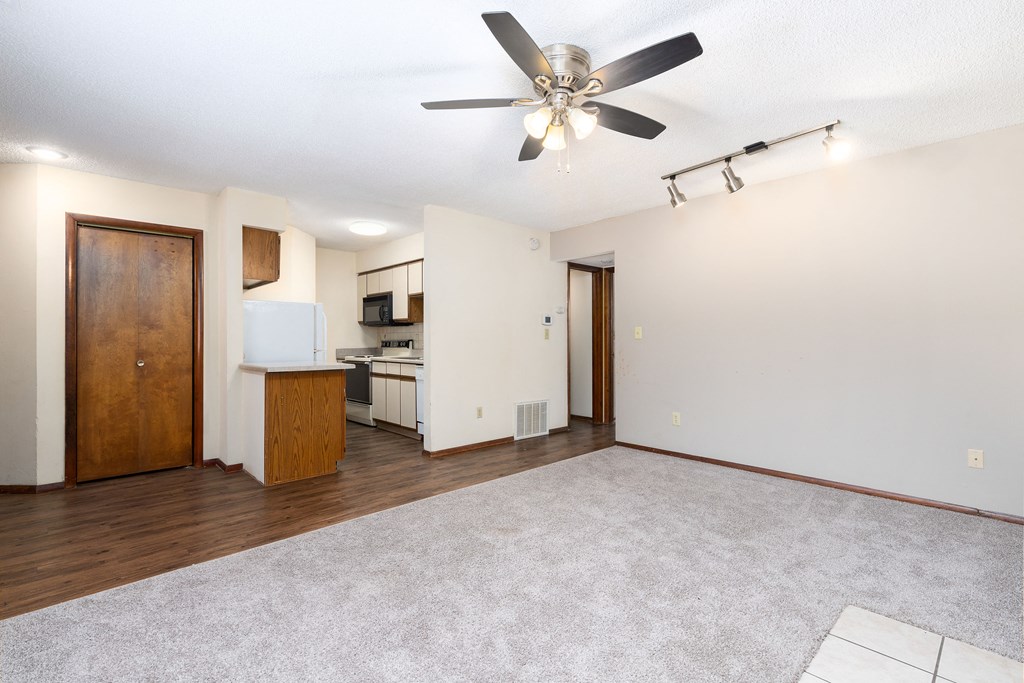 an empty living room with a ceiling fan and a kitchen