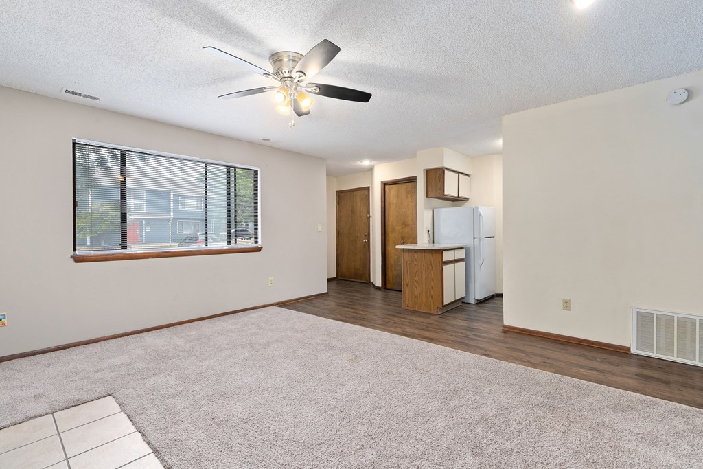 an empty living room with a ceiling fan and a kitchen