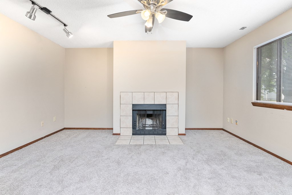 an empty living room with a fireplace and a ceiling fan