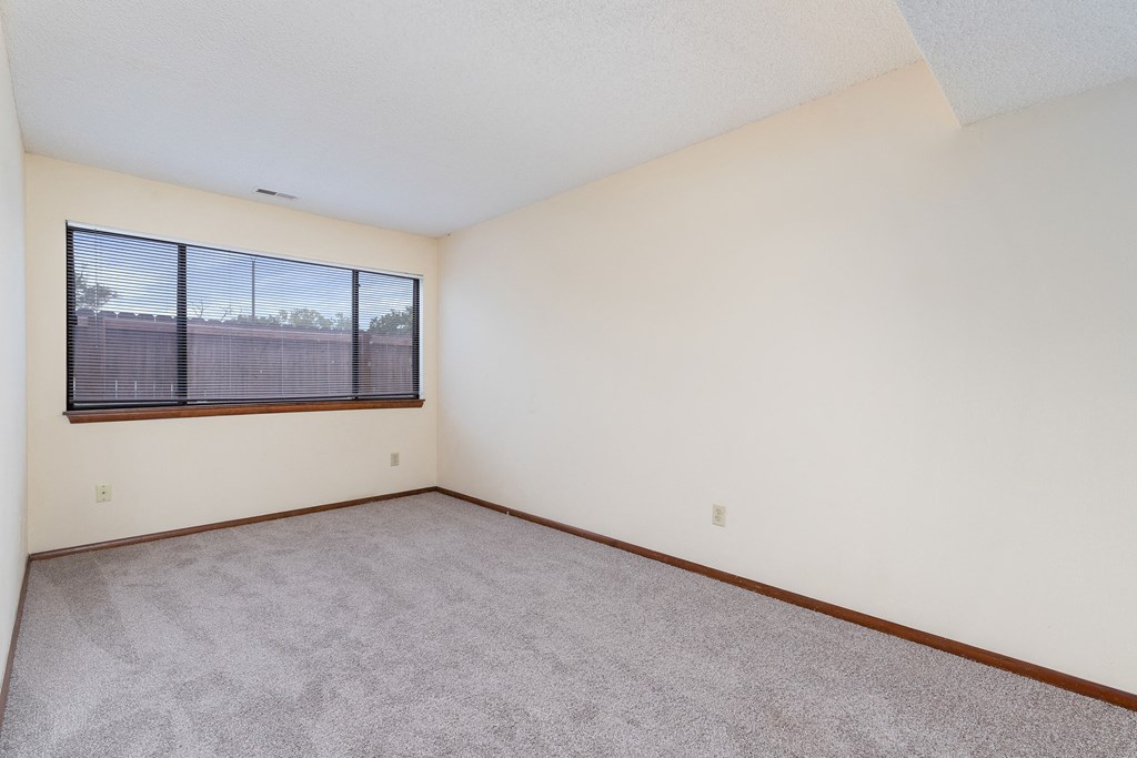 the living room of an apartment with carpet and a large window