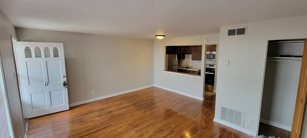 an empty living room with a kitchen in the background