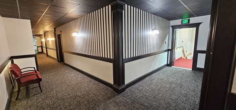 A hallway with a red chair and a green exit sign.