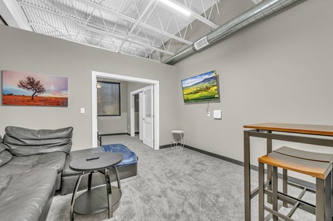 A living room with a grey couch, a round table, a television, and a painting on the wall.
