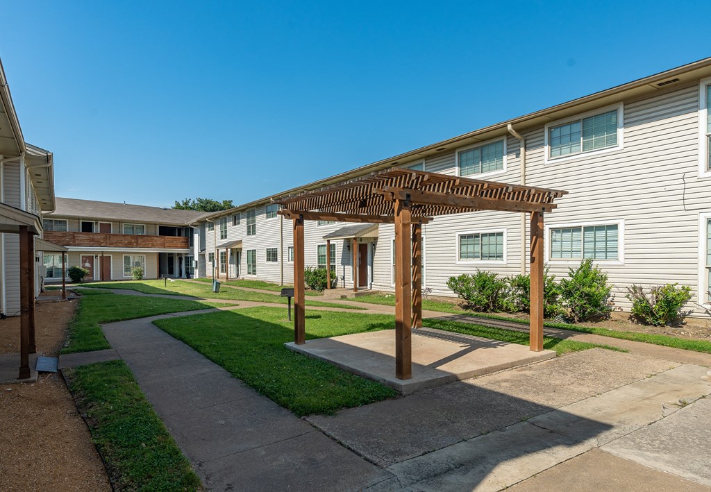 a pathway between two apartment buildings with a wooden pergola