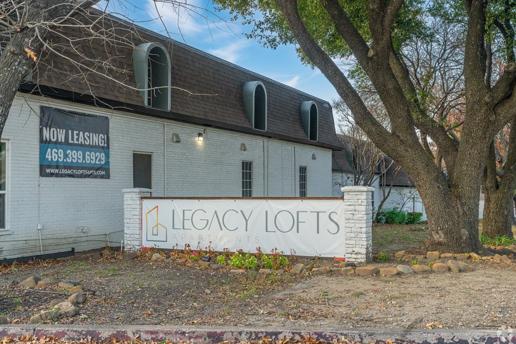 A white building with a sign that says "Legacy Lofts" is for lease.