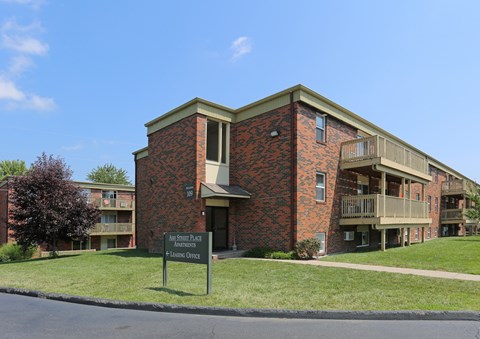 a red brick apartment building with a green lawn and a sign in front
