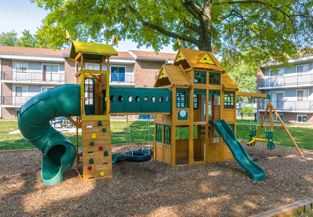 a playground with a slide and climbing wall in front of an apartment building