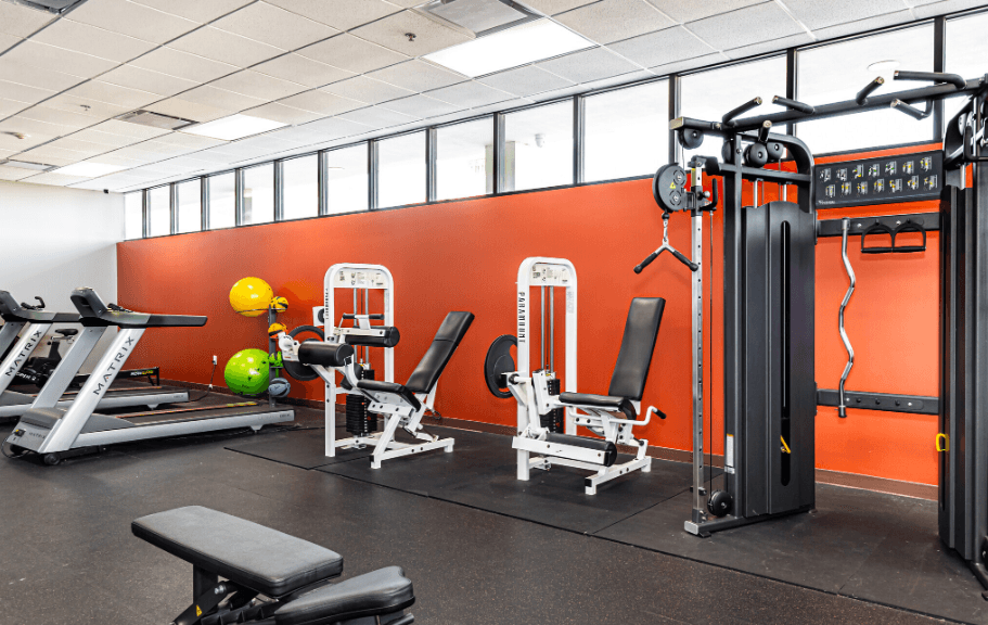 a gym with weights and other exercise equipment in front of a orange wall