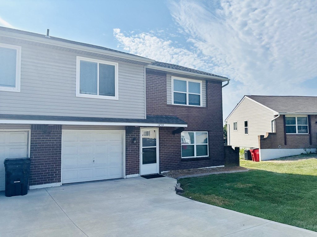 A house with a grey garage door and a red trash bin.