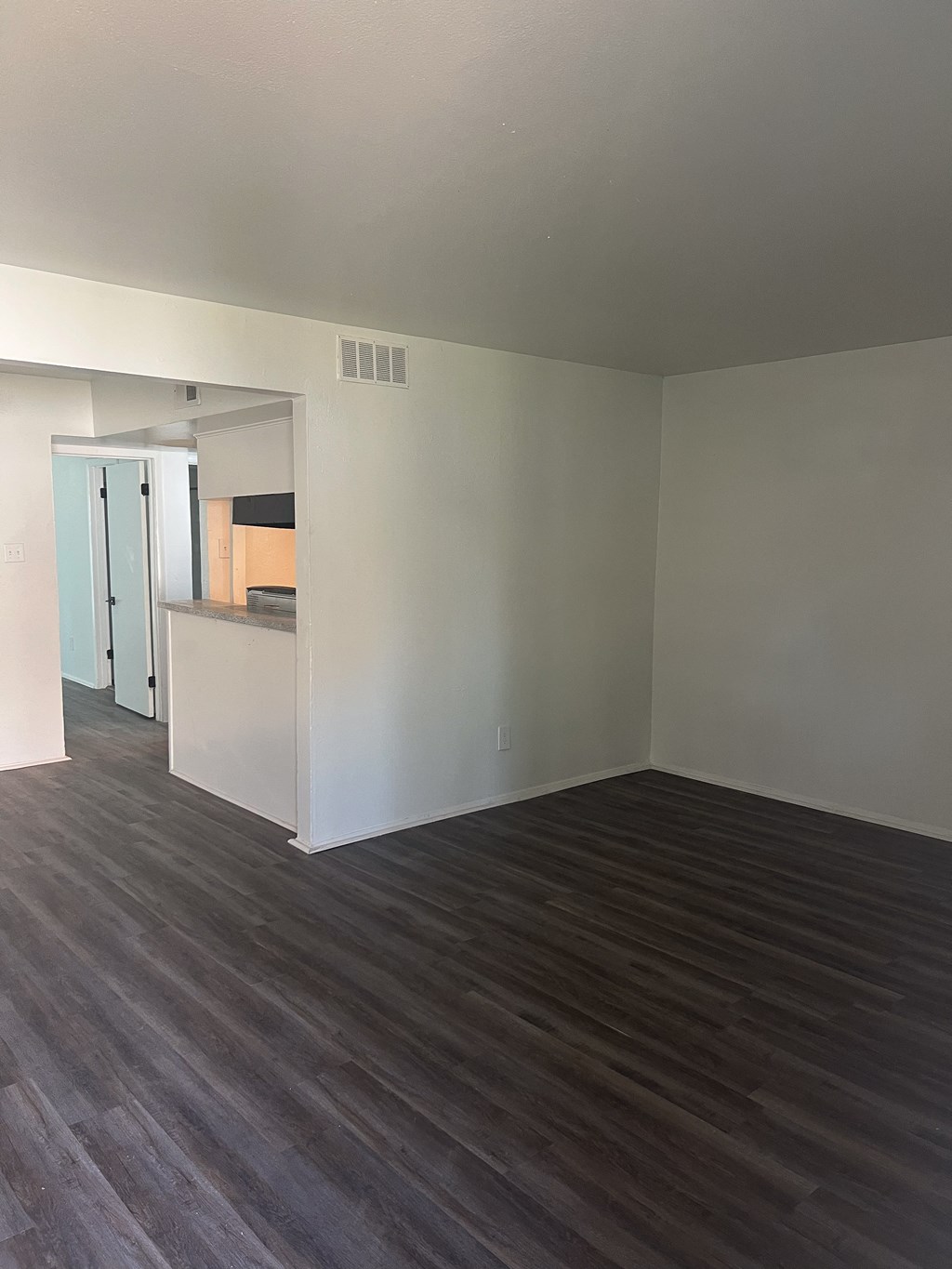 an empty living room with wood floors and a kitchen