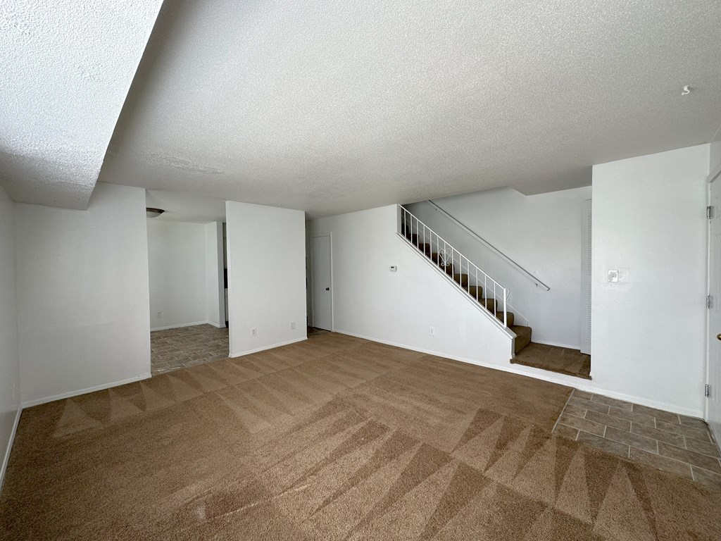 a living room with a carpeted floor and a staircase in the background