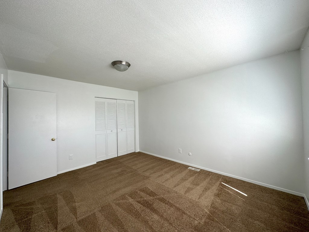 a bedroom with white walls and a brown carpet