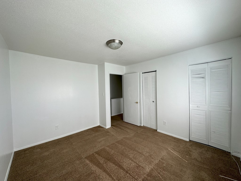 a bedroom with white walls and a brown carpet