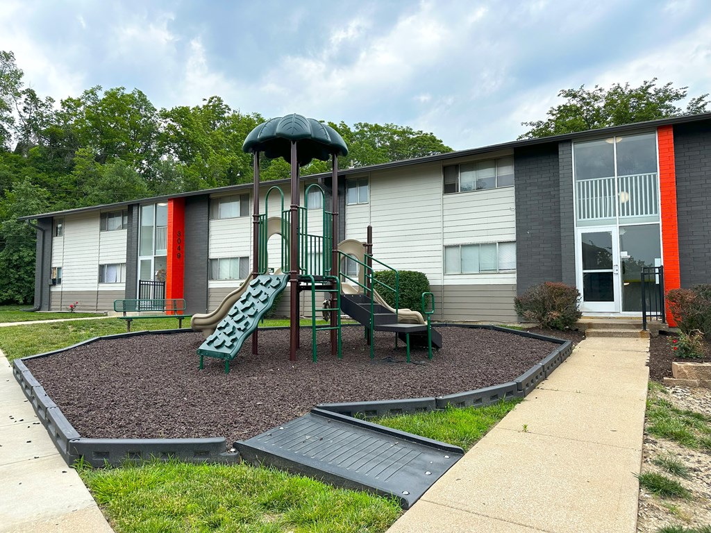 a playground with a slide and chairs in front of a building