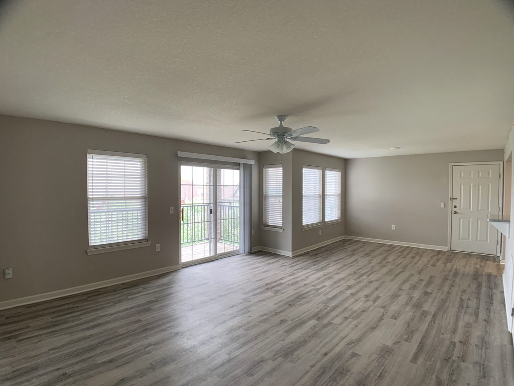 Living room with windows, patio door, and ceiling fan at Saddlewood in Olathe, KS