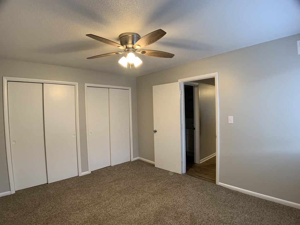 carpeted bedroom with two sliding closet doors and ceiling fan