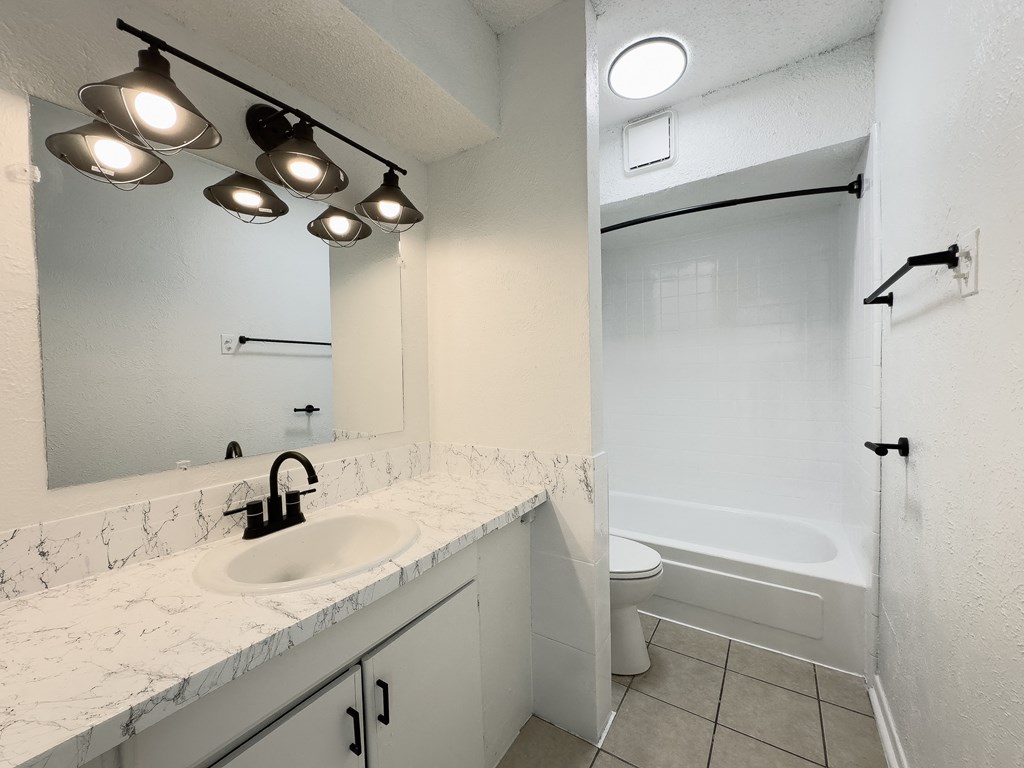 A white bathroom with a sink, mirror, and bathtub.