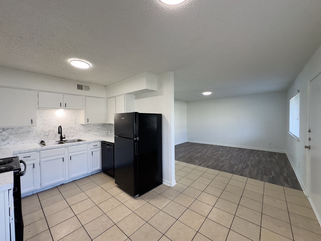 A black refrigerator in a kitchen with white cabinets and a marble backsplash.